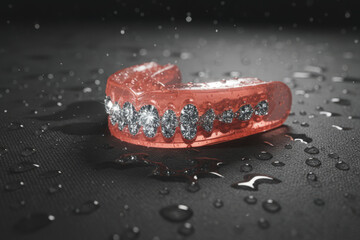 Red sport mouthguard with braces design and water drops on dark background. Dental gum shield for boxing fight protection and mma training safety equipment
