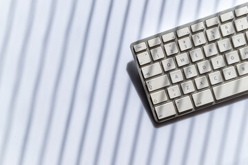 White computer keyboard on desk with dramatic shadow stripes, minimal design, clean workspace and contemporary light pattern.