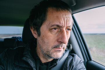 Pensive middle aged man inside a car, focused expression while driving, realistic lifestyle portrait with natural daylight and shallow depth of field.