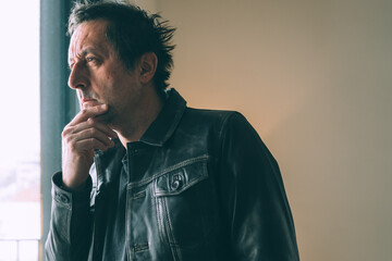 Thoughtful man in leather jacket gazing out window in soft natural light