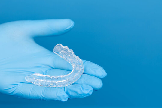 Dentist hands in gloves holding transparent dental mouth guard for night sleep, bruxism and teeth grinding prevention, orthodontic protection device on blue background, medical care and hygiene