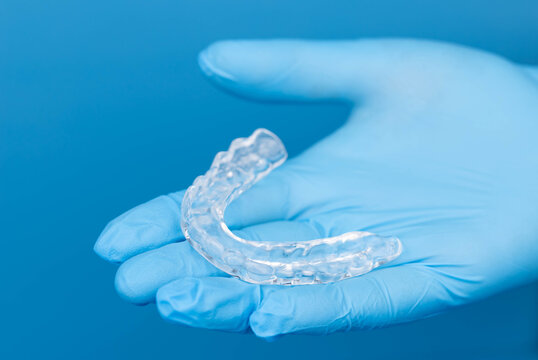 Dentist hands in gloves holding transparent dental mouth guard for night sleep, bruxism and teeth grinding prevention, orthodontic protection device on blue background, medical care and hygiene