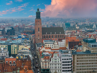 Obraz premium Aerial view of central Wroclaw, Poland, centers on the Gothic Church of St. Elizabeth, its brick tower and tiled roof rising above Old Town under pink evening clouds.