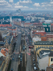 Obraz premium Aerial view of central Wroclaw, Poland shows tram lines on a broad boulevard, red tiled roofs, modern blocks, and towers under a cool partly cloudy midday sky.