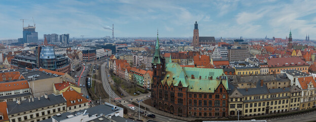 Obraz premium Aerial view of central Wroclaw, Poland, shows St. Elizabeth's tower, red rooftops, tram lines, Oder River, Gothic brick with green copper roof, and cranes on a clear day.