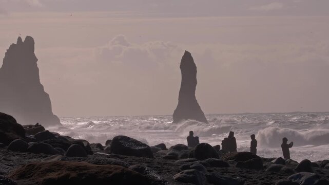 Tourists explore Reynisfjara beach with basalt columns and rough waves