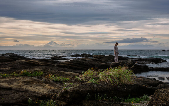 A woman contemplating in the sea breeze on a dusk coast.