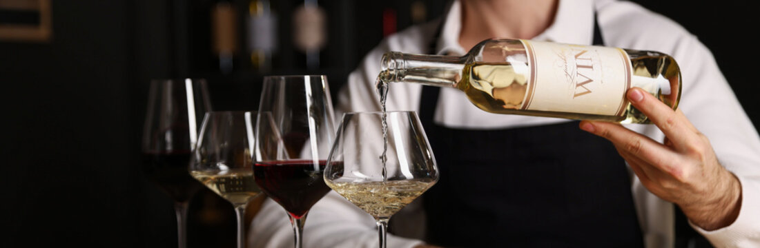 Professional sommelier pouring white wine into glass indoors, closeup