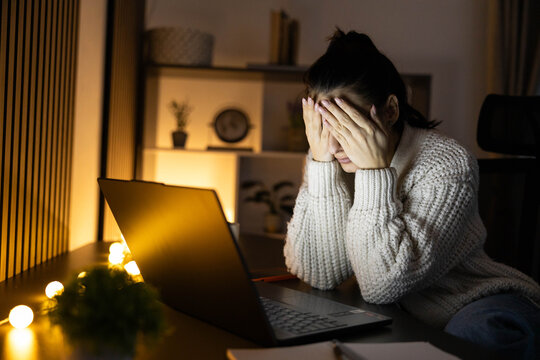 A person showing frustration while working late at a computer in a softly lit room.