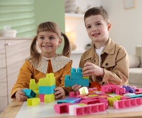 Little brother and sister playing with building bricks at wooden table indoors