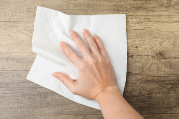 Woman wiping wooden table with paper towel, top view