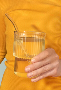 Hand holding a glass of water with a straw wearing yellow clothes.