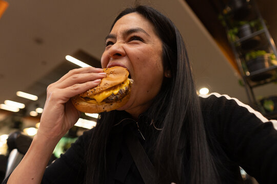 Woman Enjoying a Delicious Burger in a Lively Dining Setting