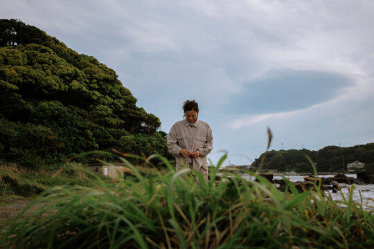 A woman bowing her head to button her coat in the sea breeze.