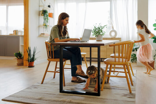 Mother working from home while her daughters playing in living room