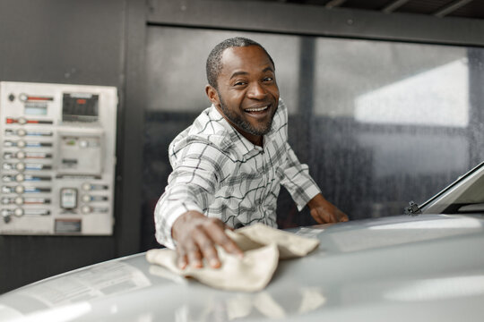 Middle aged black man wiping his car with a rag outside in the car wash