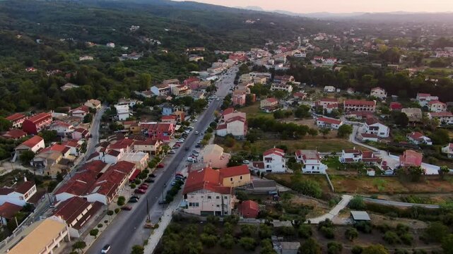 Aerial Sunset View of Acharavi Village in Corfu Greece with Long Straight Road and Mountains in Background During Golden Hour Twilight