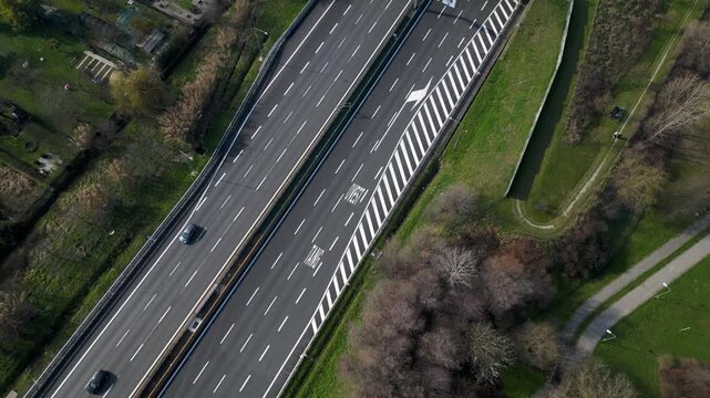 Overhead perspective of a modern highway with multiple lanes cutting through a green, vibrant landscape, revealing the flow of vehicles and the essence of transportation.