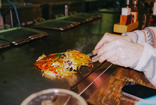 Woman eating okonomiyaki in teppanayaki restaurant in Osaka 