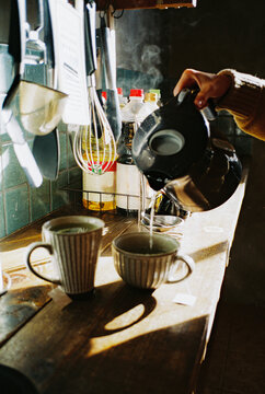 Close up of woman's hand pouring hot water in cups to brew tea 