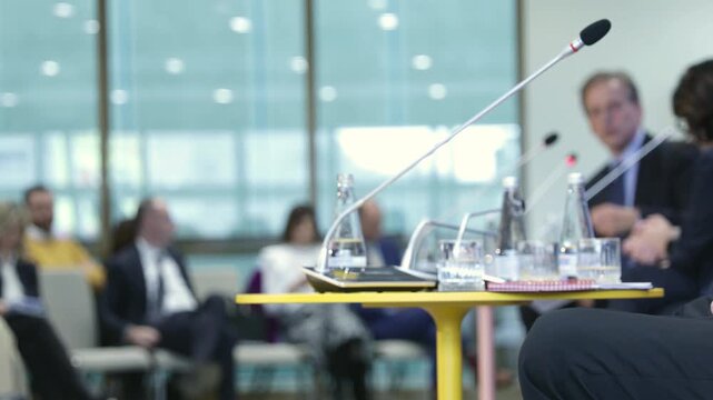 Modern business conference roundtable panel discussion with microphones and a blurred audience, featuring a professional corporate meeting interior during a seminar or workshop