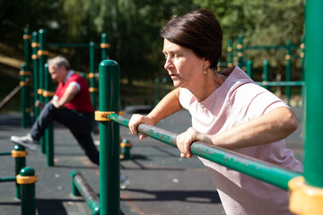 Obraz premium elderly woman performs exercises on horizontal bars in an outdoor sports area