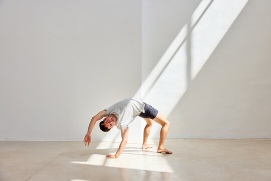 Person performing an acrobatic stretch in a bright, minimalist s