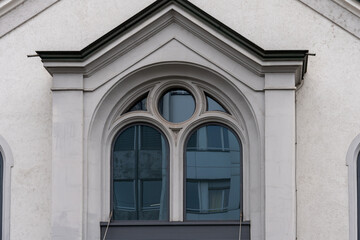 Obraz premium Part of facade of an older building with church like windows. Reflection in the windows of other buildings.