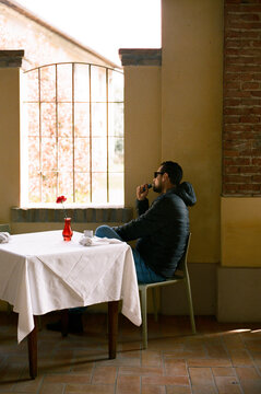 Rear sight of man sitting alfresco at table and smoking e-cigarette