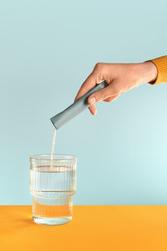 A hand dissolving a sachet with powder supplements in a glass of water