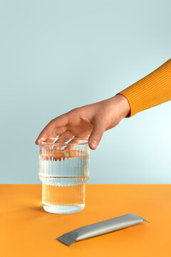 A hand taking a glass of water with collagen and vitamins from a table