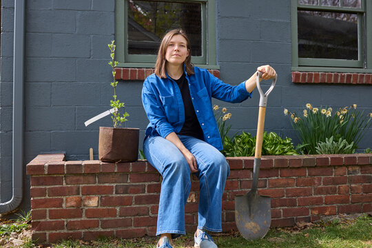 Woman sitting on the brick garden bed with a plant 
