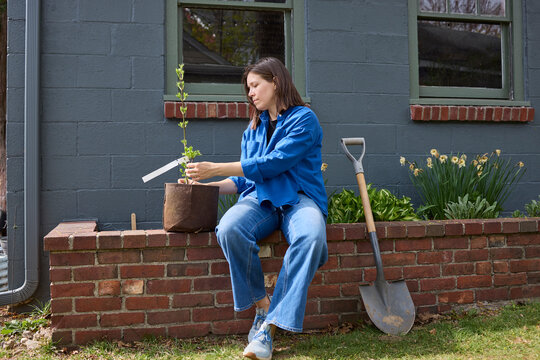 Woman sitting on the brick garden bed with a plant 