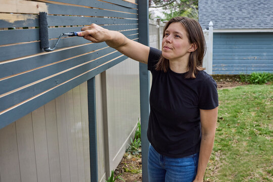 Woman painting a fence outside dark