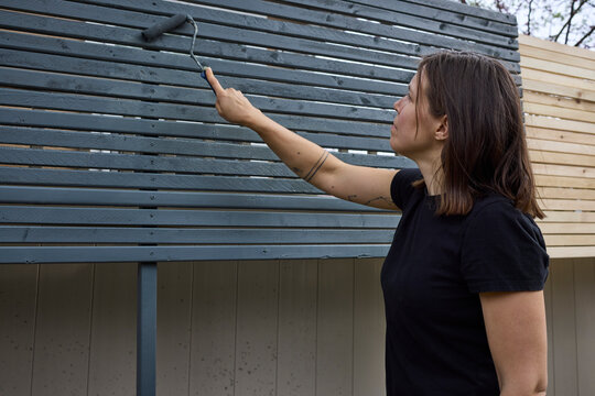 Woman painting a fence outside dark