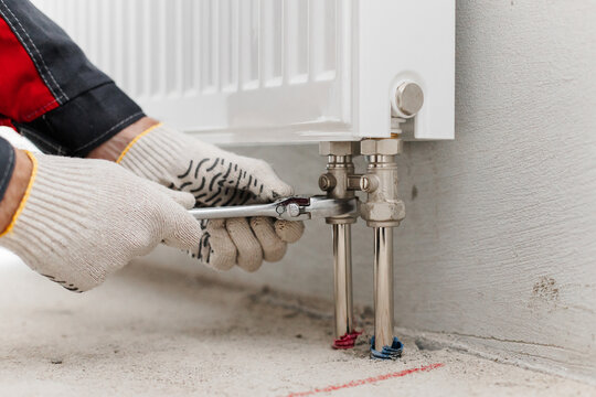 Closeup Of Hands Tightening Radiator Valve With Wrench. Plumbing Task During Heating System Assembly.