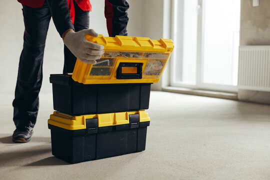 Worker Opening Top Tool Case Stacked On Second Case In Empty Room. Organization Of Construction Supplies On Site.