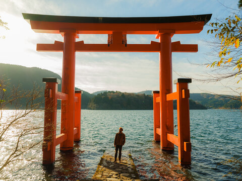 Man standing near red tori gates on Lake Ashi in autumn 