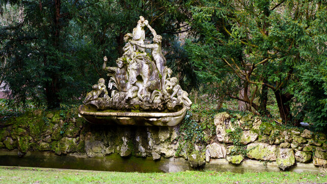 Elegant stone fountain with cascading water flows stands as a park centerpiece. Sculpted details and gentle splashes create a soothing sound amid surrounding greenery. Soft daylight reflects on rippli