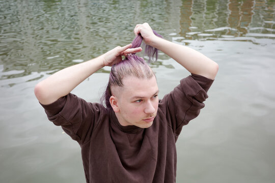 Man Ties up Long Purple Hair by the Water 