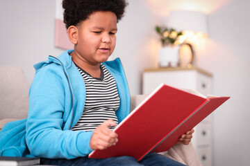 Naklejka premium Boy reading book on sofa at home