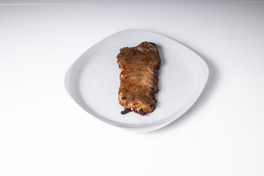 Single grilled flank steak displaying delicious brown crust, ready for eating as a healthy and protein rich meal on a square white ceramic plate against a clean white background