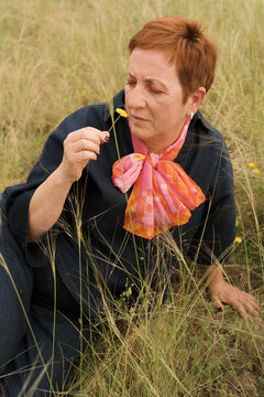 Woman smelling a flower in a grassy field during daytime