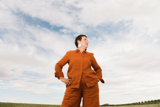Confident woman poses against a cloudy sky outdoors