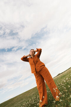 Woman in orange outfit poses in open field under a bright sky