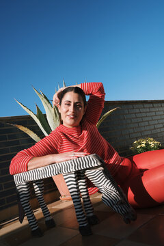Woman poses with striped stool against a clear blue sky