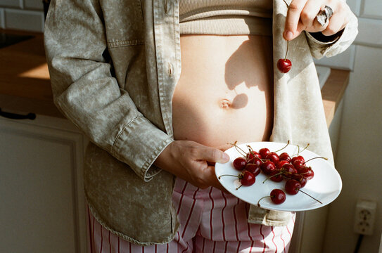 Woman holding cherries on a plate while showcasing her pregnancy bump