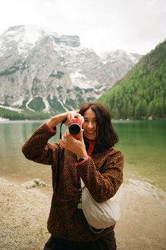 Woman holding camera by lake in the Dolomites, facing forward