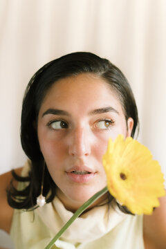 Young woman with a yellow flower poses against a light background