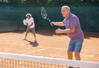 Two men of different ages playing tennis together in the open air. Men team hits tennis balls with a racket
